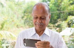 Older Indian man playing at an online casino on his smartphone. Wearing a striped shirt, smiling and looking down.