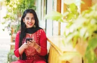 Indian woman playing at an online casino on her smartphone. Wearing a red sari and black scarf, smiling and looking up.